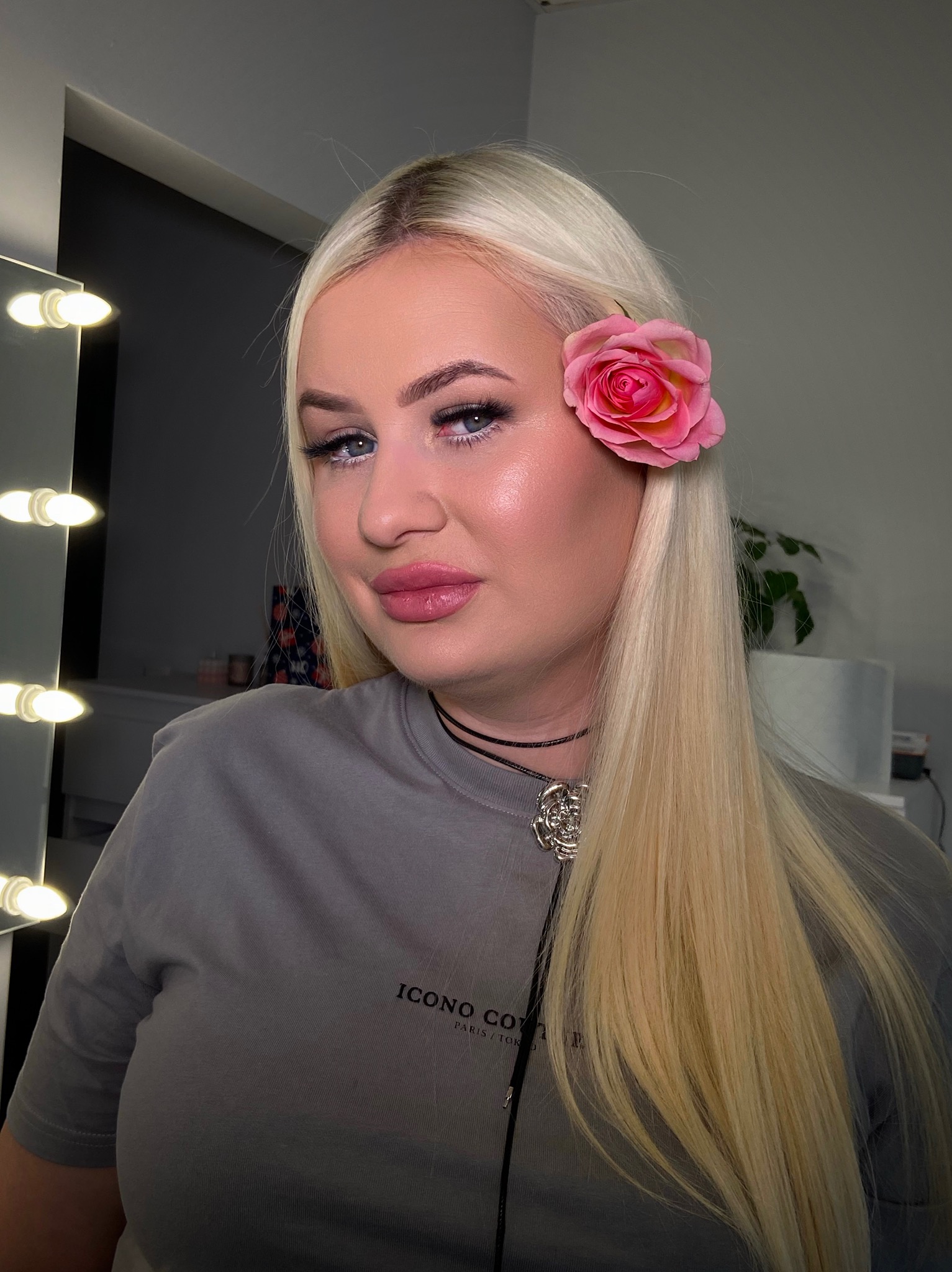 Portret kobiety z blond włosami i różą we włosach, wizaż z błyszczącym wykończeniem, subtelna biżuteria, oświetlenie studyjne z lustrem.