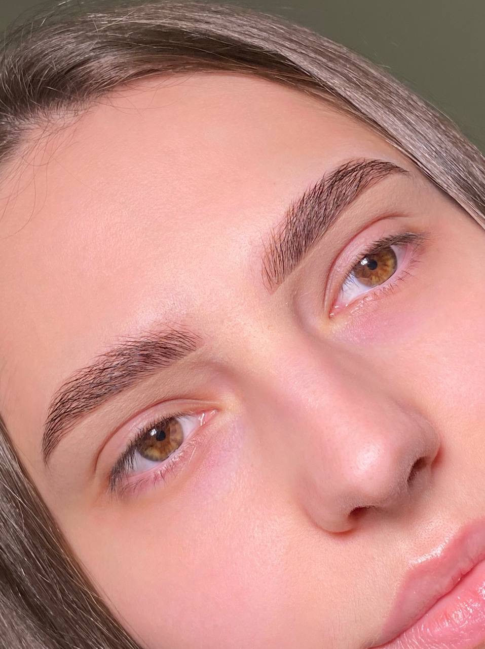 Zbliżenie na brwi po zabiegu laminacji. Widoczne idealnie ułożone, ciemne włoski i naturalny efekt. Modelka ma jasną cerę i brązowe oczy.