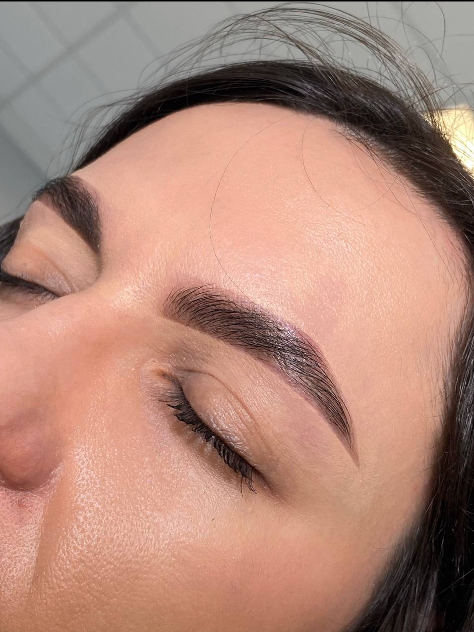 Zbliżenie na kobiecą twarz po zabiegu laminacji brwi. Widoczne ciemne, idealnie ułożone brwi z efektem lekkiego połysku.