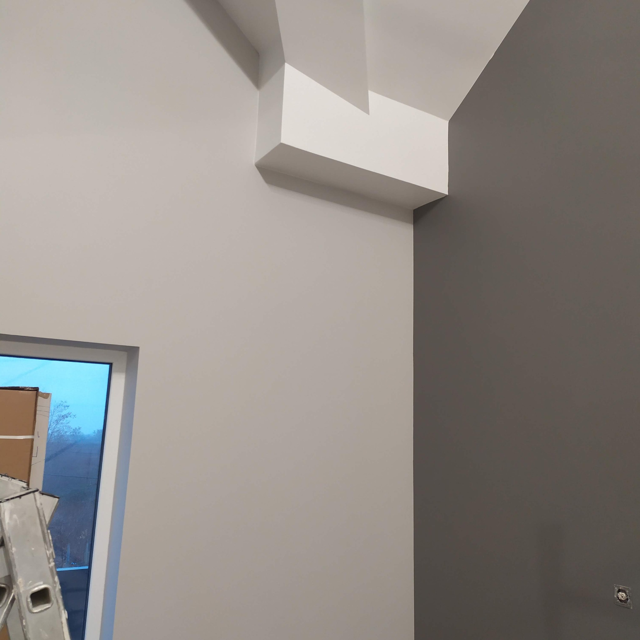 Pomieszczenie po malowaniu ścian na dwa kolory: jasnoszary i grafitowy. Widoczne elementy dekoracyjne na suficie i drabina malarska przy oknie.