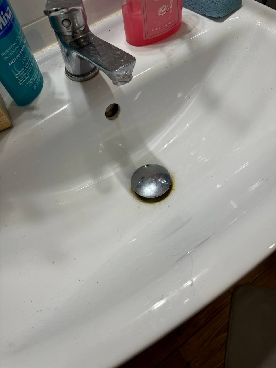 Zlew łazienkowy z armaturą, widoczne ślady użytkowania i osady. Na powierzchni zarysowania i drobne zabrudzenia, brak świeżości.