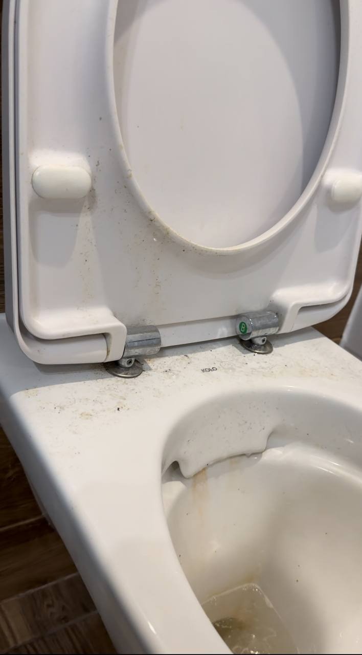 Z bliska: mocno zabrudniona toaleta marki Kolo z otwartą klapą i widocznymi śladami użytkowania. Zaniedbana ceramika sanitarna.