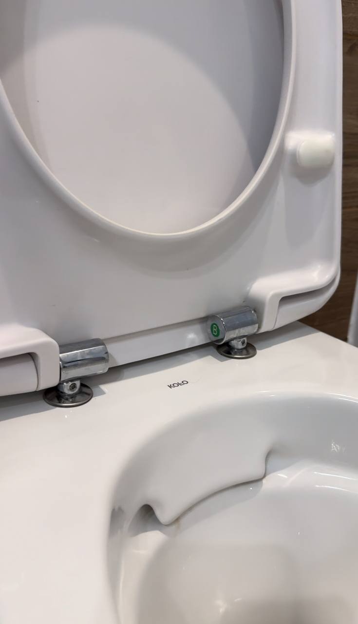 Biała, ceramiczna toaleta marki Koło z podniesioną deską, widok z bliska na zawiasy i wnętrze muszli. Czysta powierzchnia, gotowa do użytku.