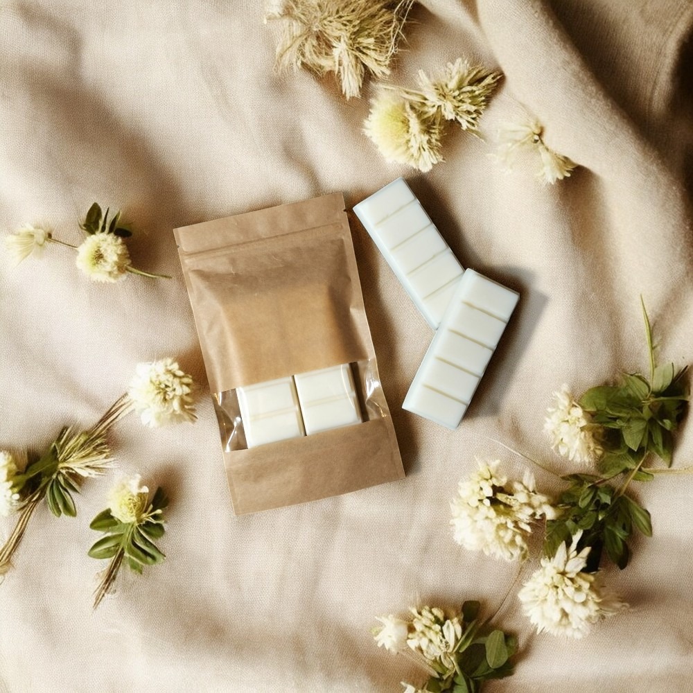 Beżowe tło z brązową torebką, woskami zapachowymi i białymi kwiatami. Stonowana kolorystyka, naturalne materiały i elegancka kompozycja.