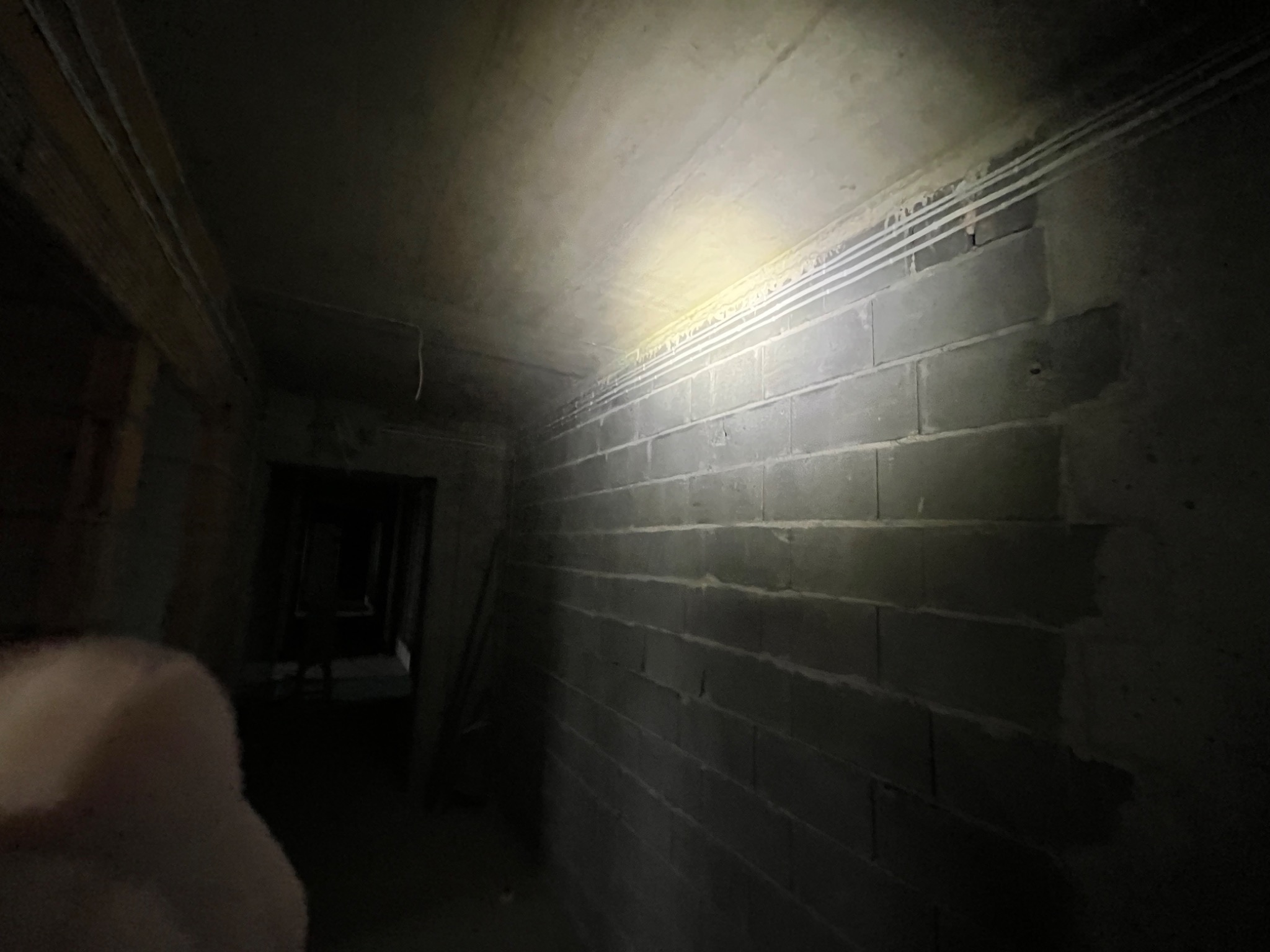 Wnętrze w surowym stanie z widocznymi przewodami elektrycznymi przy suficie w Sułoszowej. Ściany z szarego betonu, oświetlone punktowo.