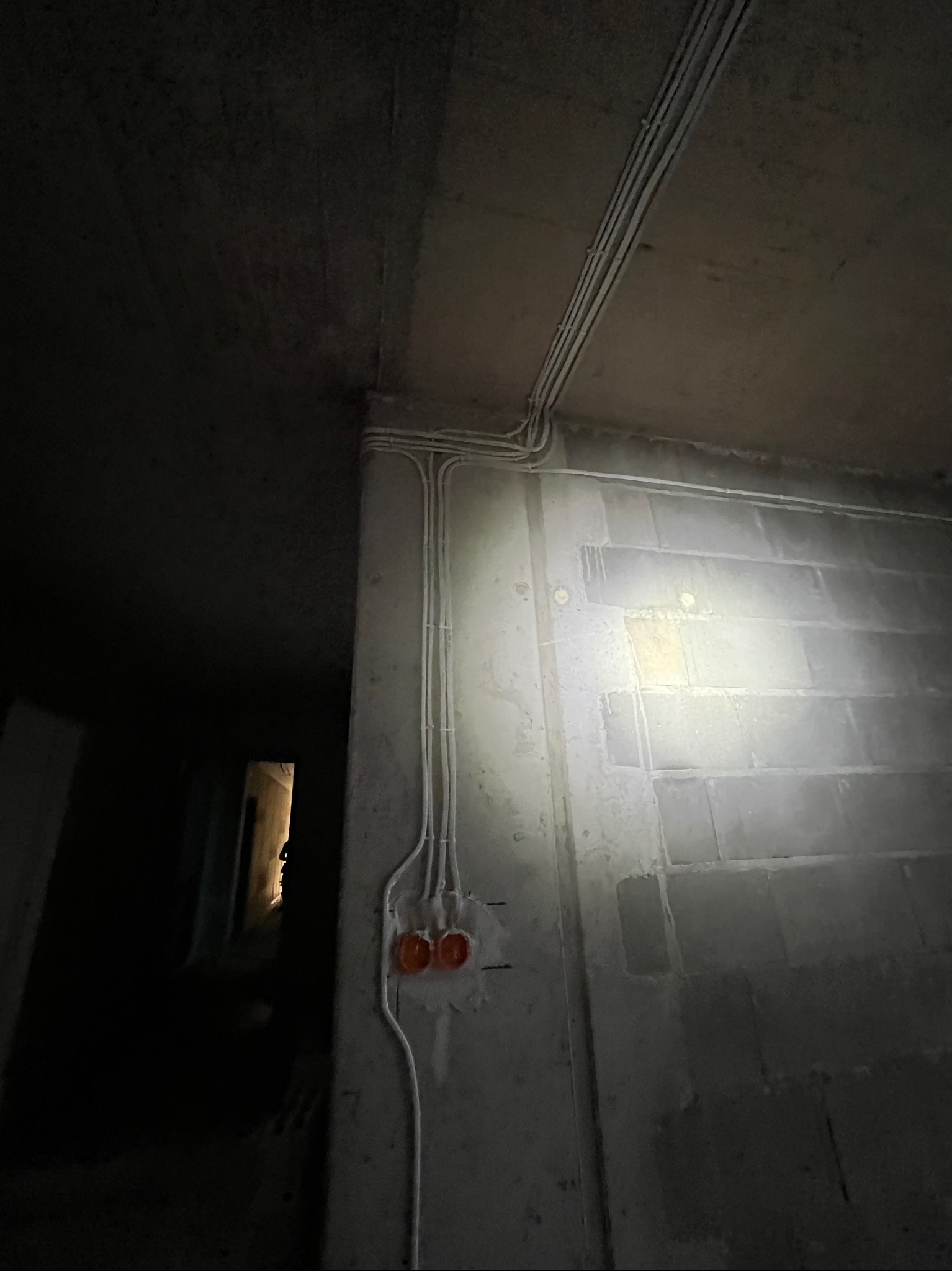 Surowy beton, kable elektryczne w peszlach, puszki pod gniazdka. Instalacja w trakcie montażu, widok z dołu, ciemne otoczenie, niedokończone wnętrze.