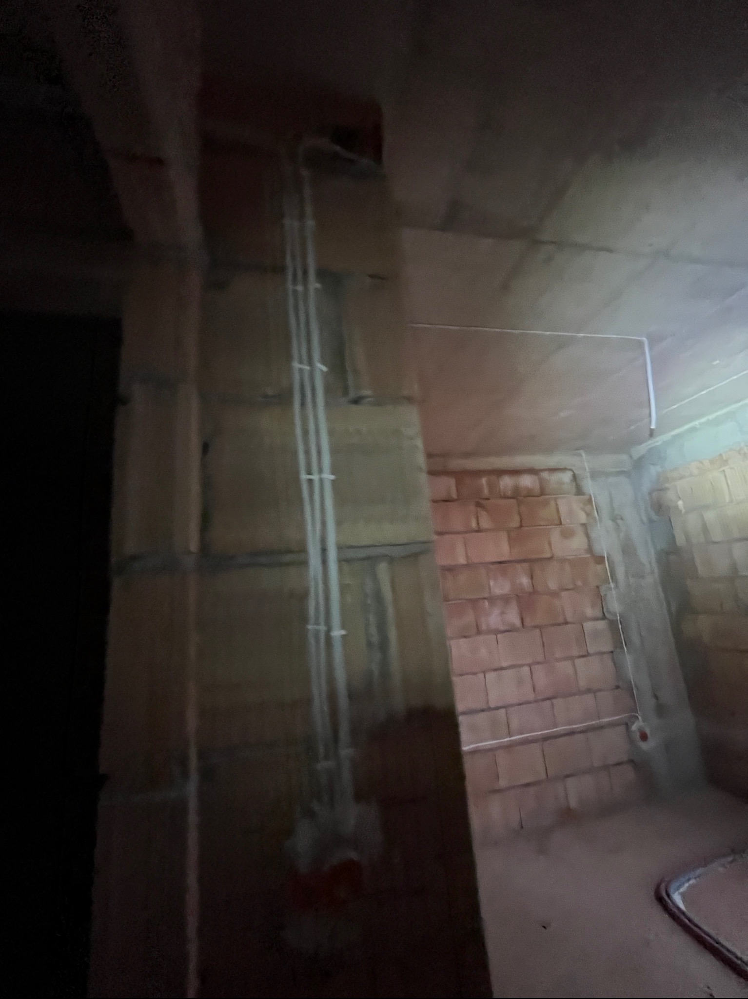 Wnętrze w trakcie prac: pionowe rury instalacji elektrycznej na ścianie z cegły, przewody pod sufitem. Surowy stan, brak wykończenia.