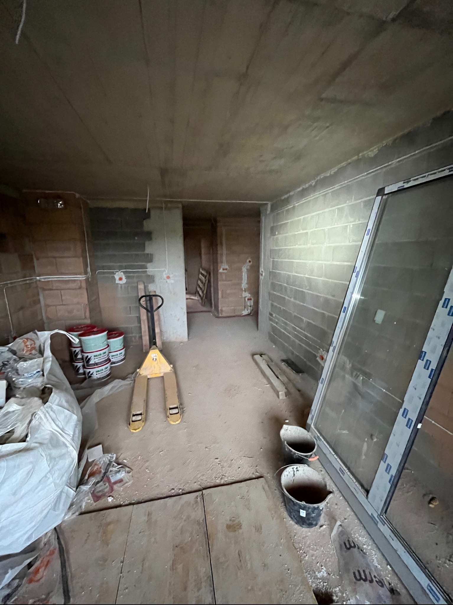 Wnętrze w trakcie prac wykończeniowych: widoczne puszki z farbą, paleciak, okno, wiadra, ściany z instalacją elektryczną. Surowy stan, przygotowanie do dalszych prac.