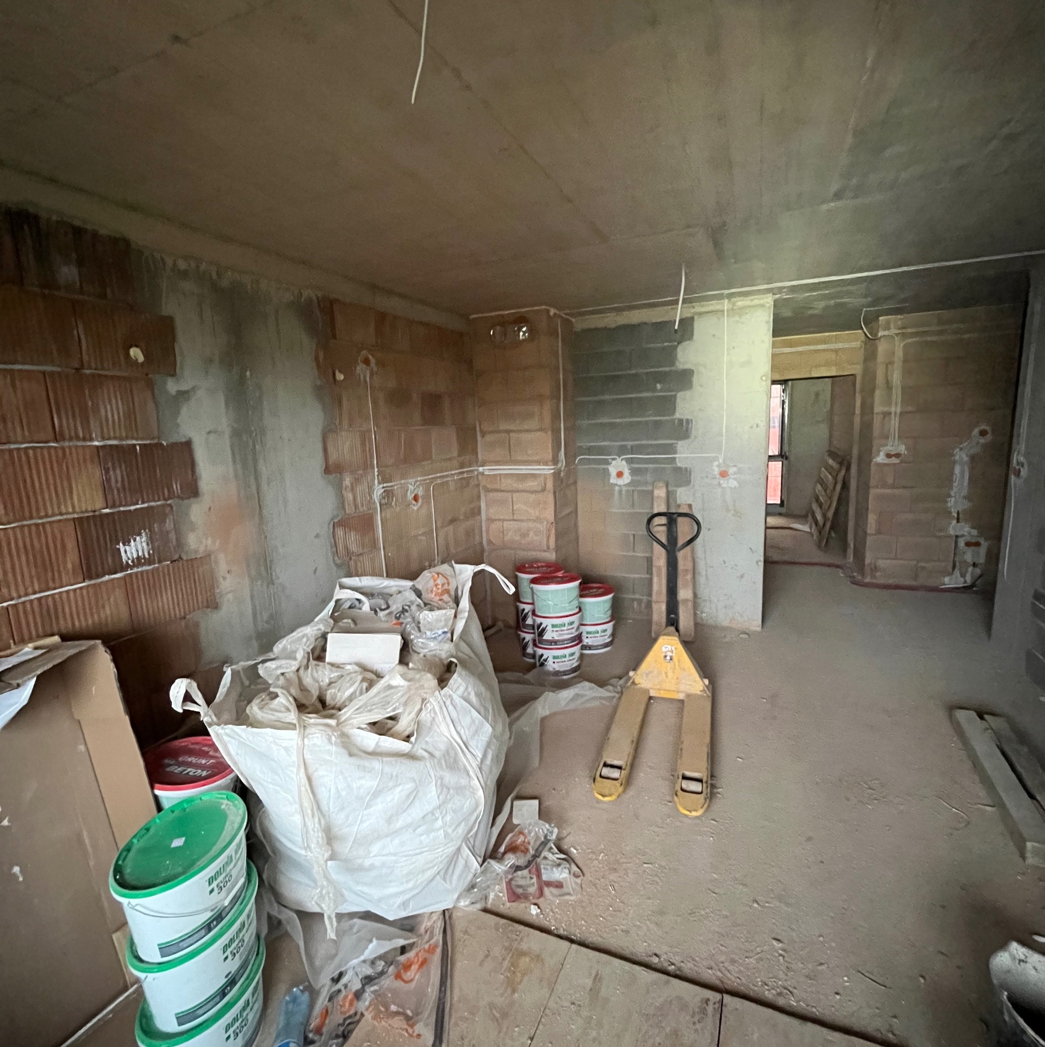 Wnętrze w trakcie prac instalacyjnych w Sułoszowa. Widoczne przewody elektryczne, puszki, materiały budowlane i paleciak.