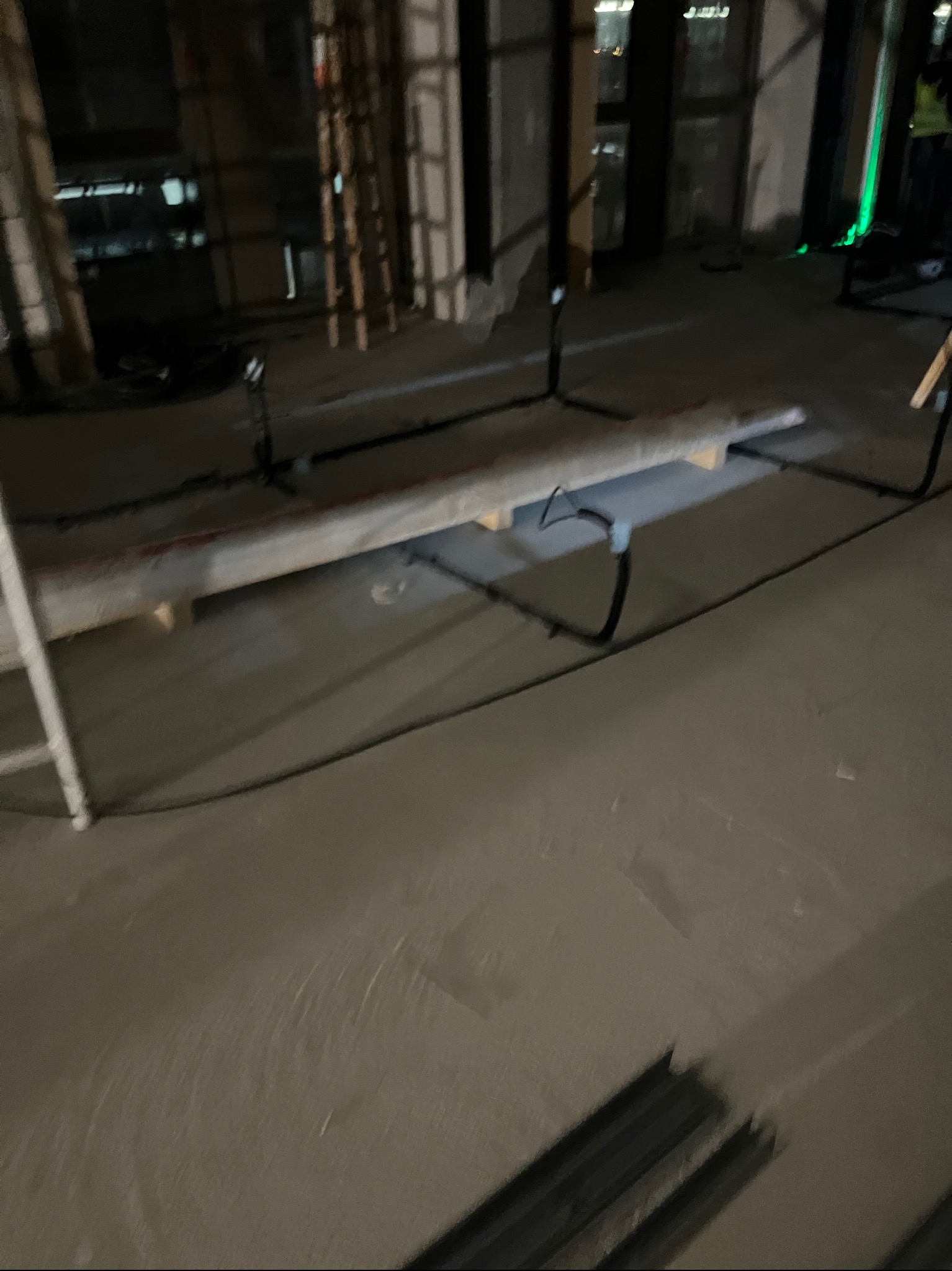 Szara podłoga z widocznymi przewodami elektrycznymi, częściowo ukrytymi pod listwą. W tle elementy konstrukcyjne budynku i okna.