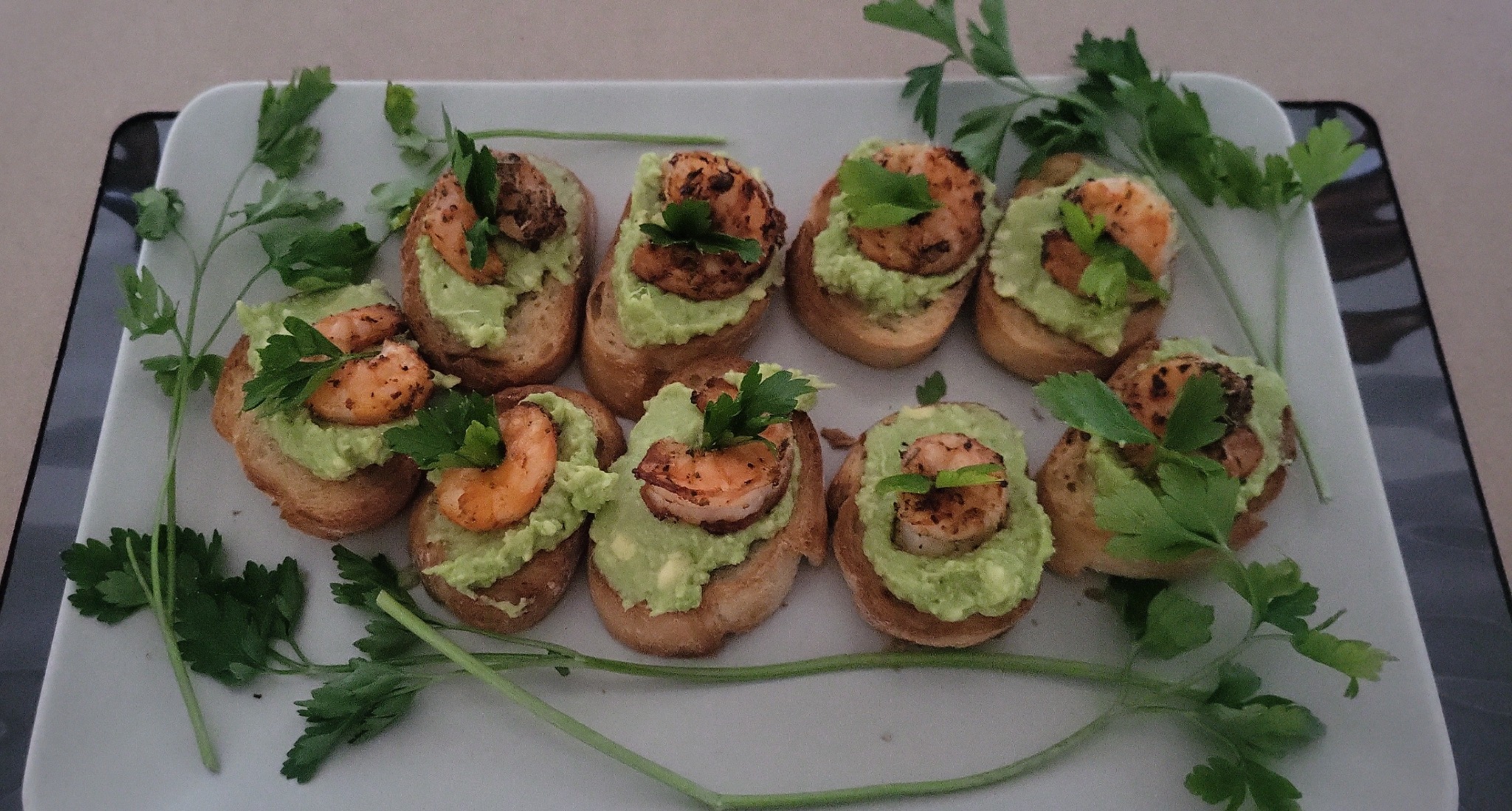 Apetizing kanapeczki z krewetkami i awokado na białym talerzu, udekorowane świeżą pietruszką. Idealne jako przekąska na przyjęciu.