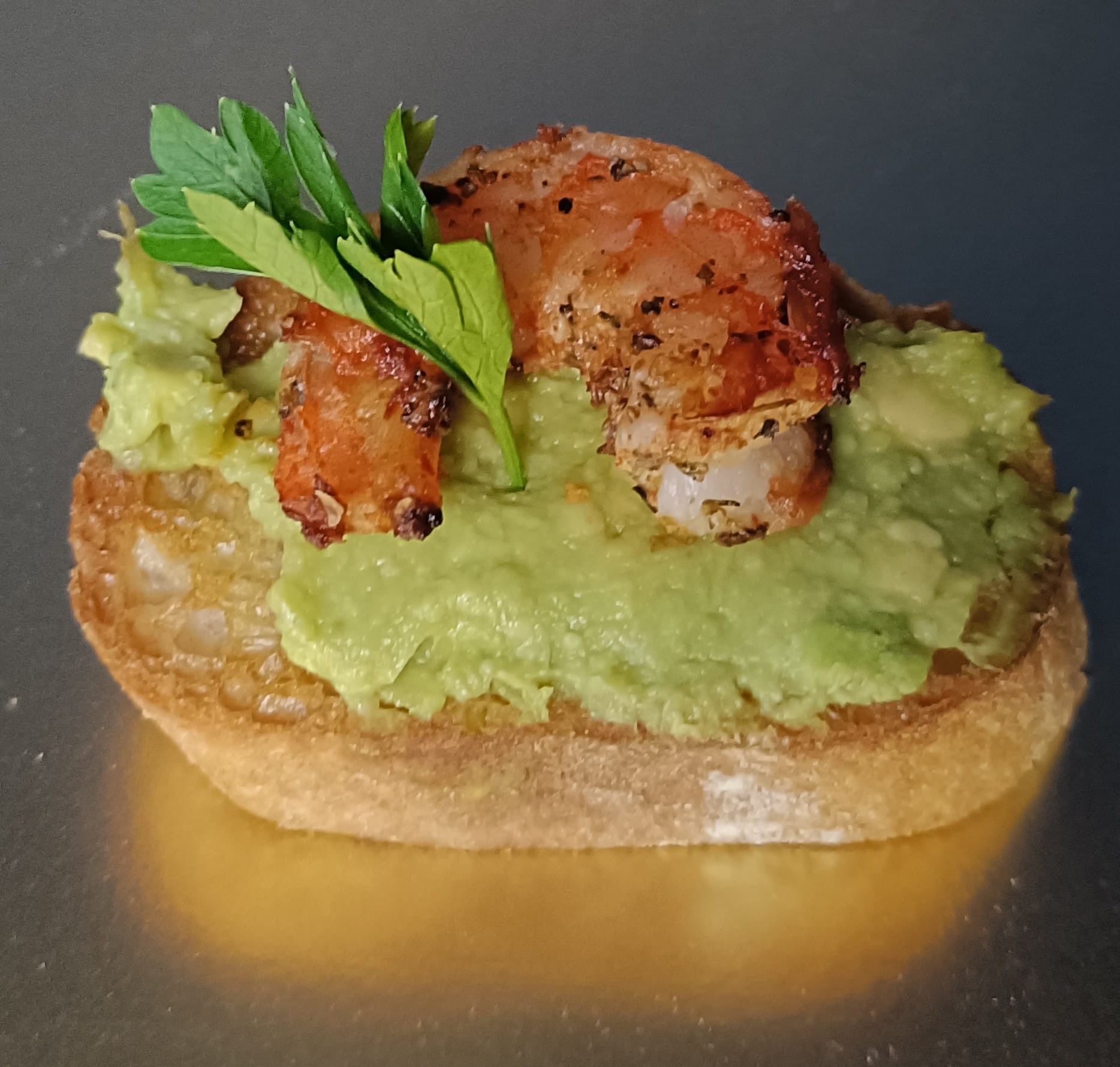 Kromka chleba z awokado, krewetką i zieloną pietruszką na błyszczącym tle. Kanapka z owocami morza, zbliżenie, ostre światło.