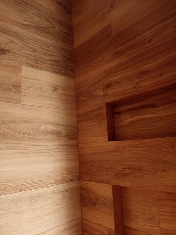 Wykończona ściana z paneli drewnopodobnych w dwóch odcieniach brązu, z wnęką. Widok na narożnik i fragment ściany obok.