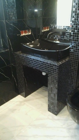 Elegancka, czarna umywalka w łazience wykończonej mozaiką i marmurem. Bidet widoczny w prawym dolnym rogu. Nowoczesny design z dbałością o szczegóły.