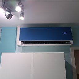 MR-KLIMA SYSTEM Robert Duszyński - Niebieski klimatyzator ścienny z wyświetlaczem temperatury 22.0, zamontowany nad białymi szafkami, oświetlony reflektorami sufitowymi.