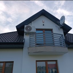 MR-KLIMA SYSTEM Robert Duszyński - Biały klimatyzator Rotenso zamontowany na ścianie domu z balkonem i anteną satelitarną. Widok z dołu na elewację budynku z ciemną dachówką.