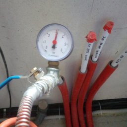 Usługi hydrauliczno-remontowe Robert Łebek - Manometr AFRISO podłączony do instalacji z rurami oznaczonymi opisami, m.in. 'ZIMNA DUZE W.C.', 'ZIMNA MAŁE W.C.', 'BOJLER'. Widoczne elementy instalacji.