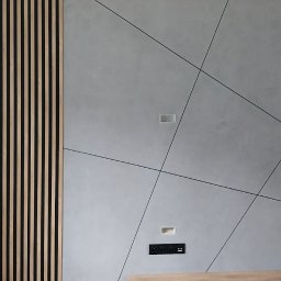Usługi hydrauliczno-remontowe Robert Łebek - Nowoczesna ściana z dekoracyjnymi panelami lamelowymi i płytami betonowymi z czarnymi liniami podziału, gniazdka elektryczne.