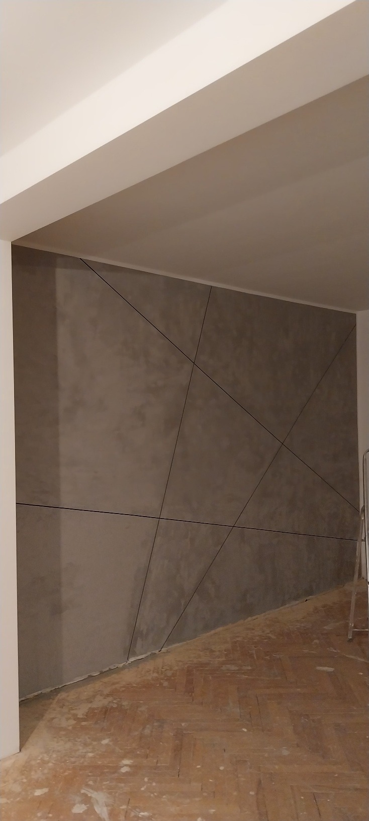 Dekoracyjna ściana z efektem betonu i geometrycznym wzorem w Lubszy. Widoczna drabina malarska, podłoga częściowo zakryta folią.