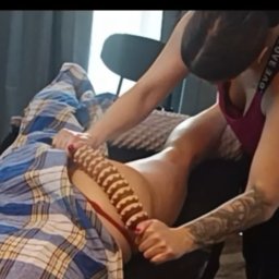 Studio Masażu Harmonia Dotyku - Masażer w akcji: masaż drewnianym wałkiem na udzie pacjenta we Wrocławiu. Masażystka z tatuażem na ramieniu wykonuje zabieg w gabinecie.