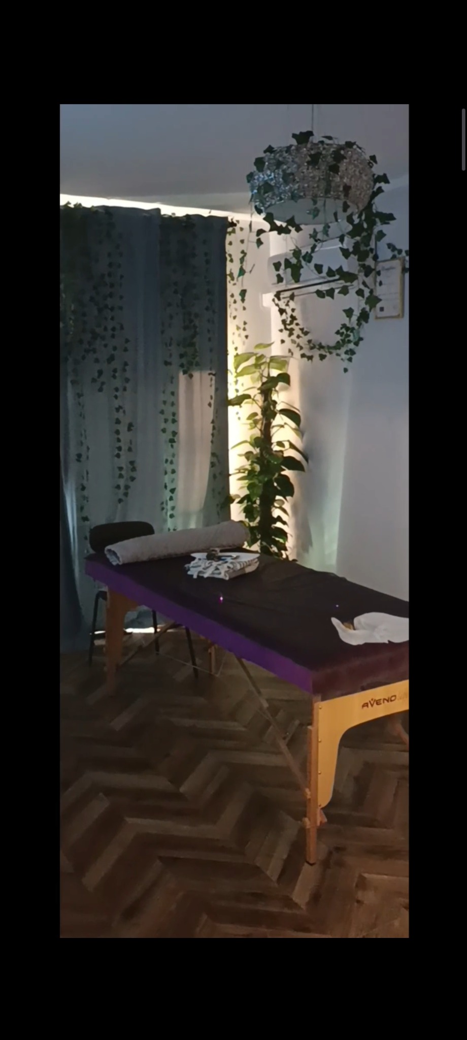 Stylowe wnętrze gabinetu z fotelem do masażu Aveno, roślinami pnącymi się po ścianach i dekoracyjną lampą sufitową, tworzące relaksującą atmosferę.