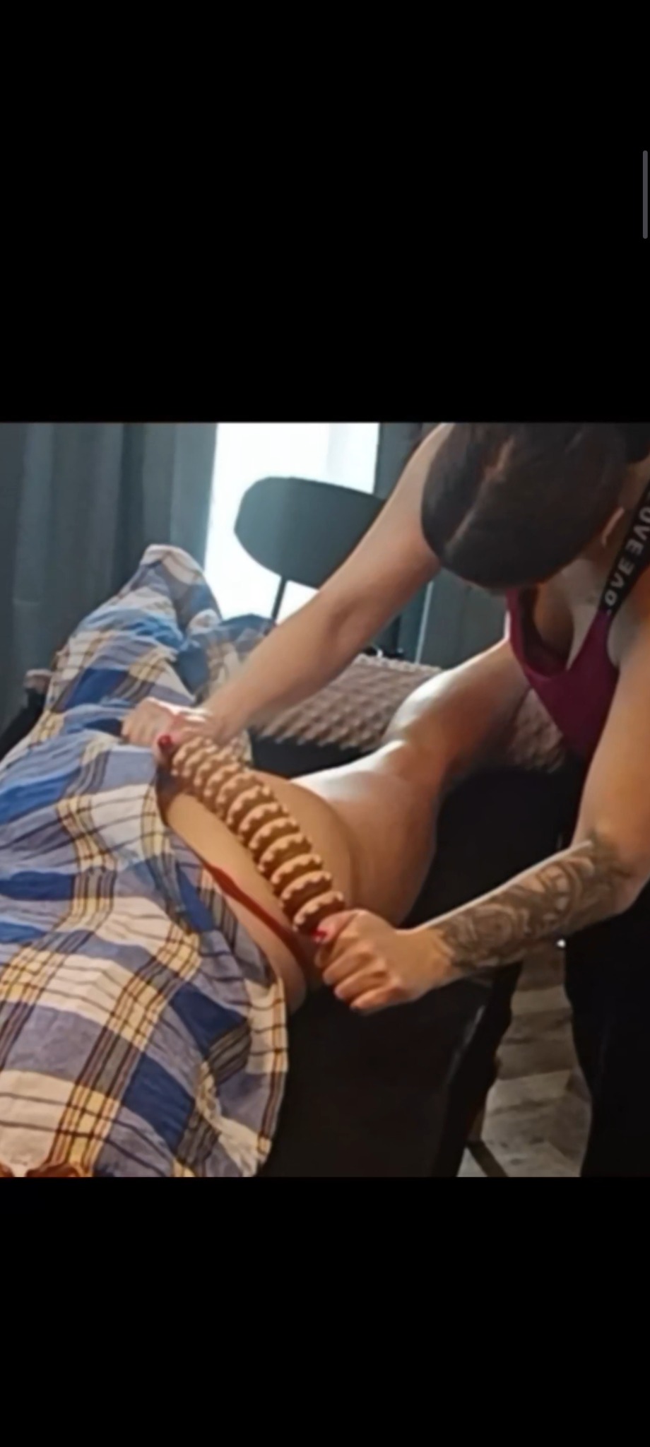 Masażer w akcji: masaż drewnianym wałkiem na udzie pacjenta we Wrocławiu. Masażystka z tatuażem na ramieniu wykonuje zabieg w gabinecie.