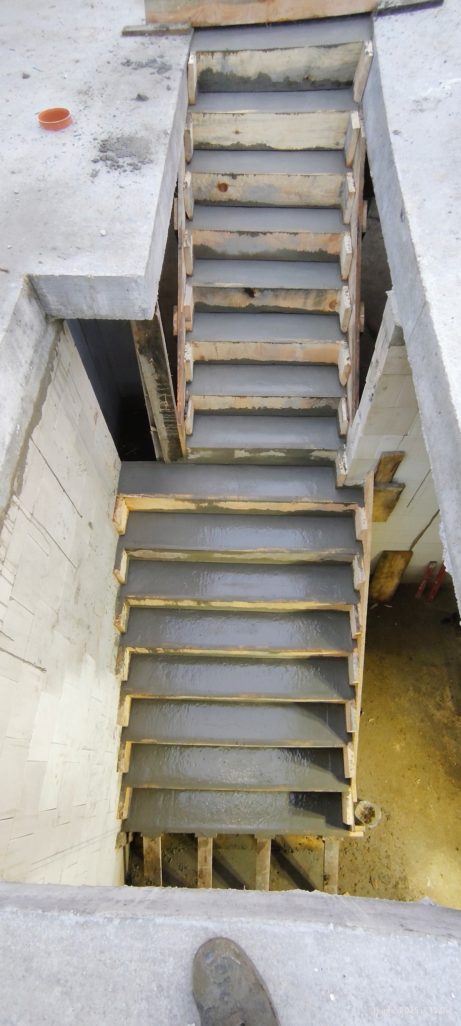 Wylane betonowe schody w surowym stanie, z drewnianym szalunkiem, widok z góry. Na dole widoczny fragment buta.