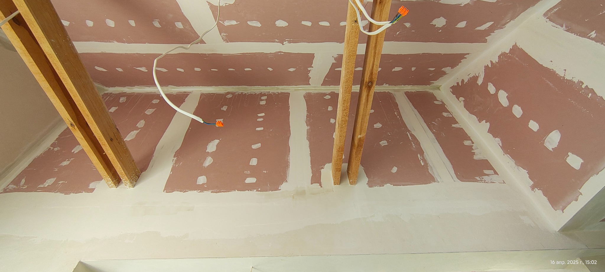 Skośny sufit z płyt karton-gips, widoczne drewniane belki i instalacja elektryczna. Szpachlowane łączenia płyt. Ujęcie z dołu, perspektywa zbieżna.