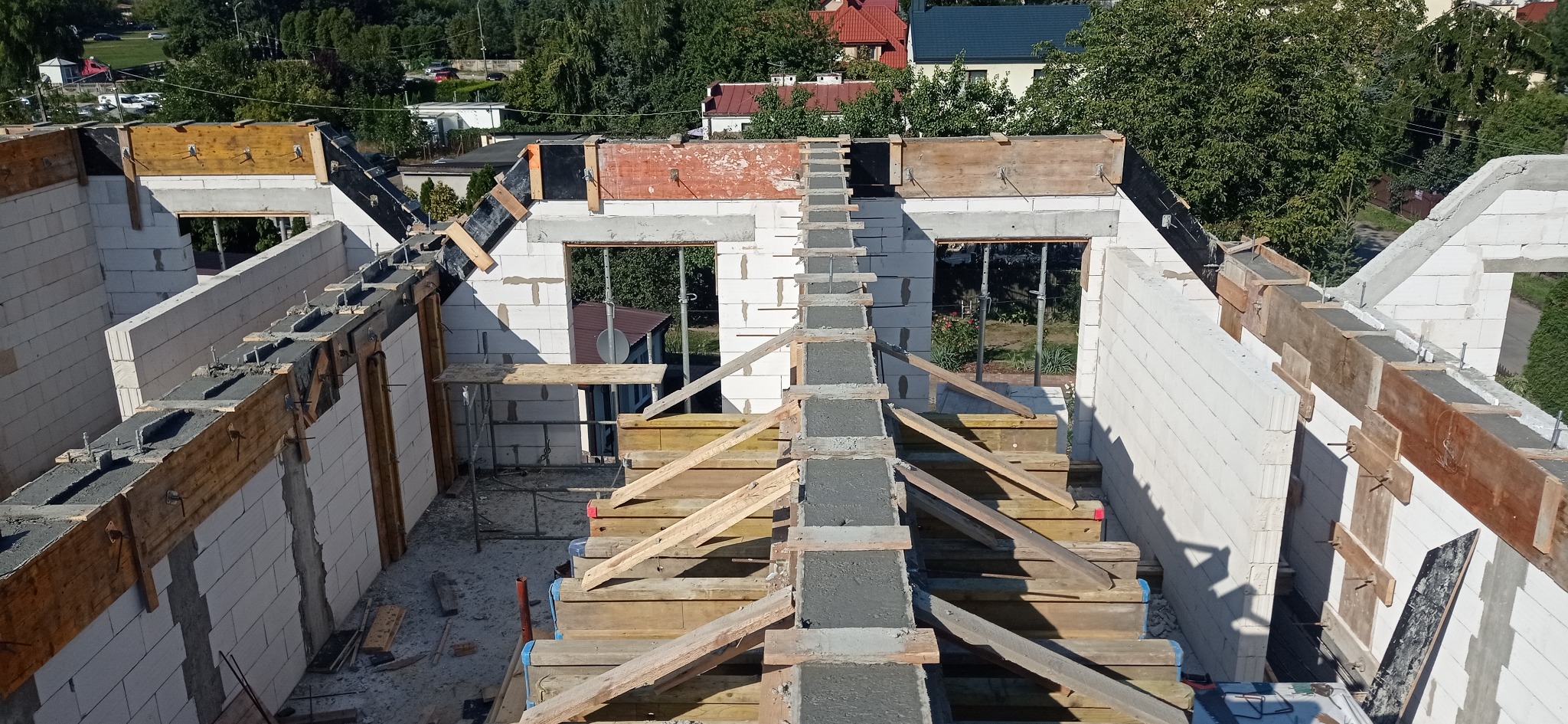 Budowa domu z betonu komórkowego: ściany z oknami, zalane betonem nadproża i słupy, drewniane szalunki. Widok z góry na plac budowy w słoneczny dzień.