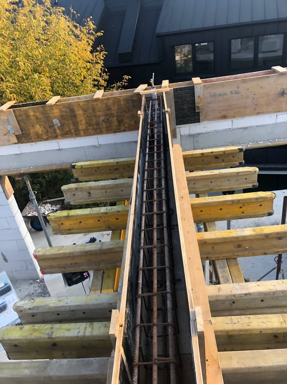 Zbrojenie pionowe w szalunku, widok z góry. Element konstrukcyjny budynku w trakcie budowy, z widocznymi elementami drewnianymi i bloczkami.