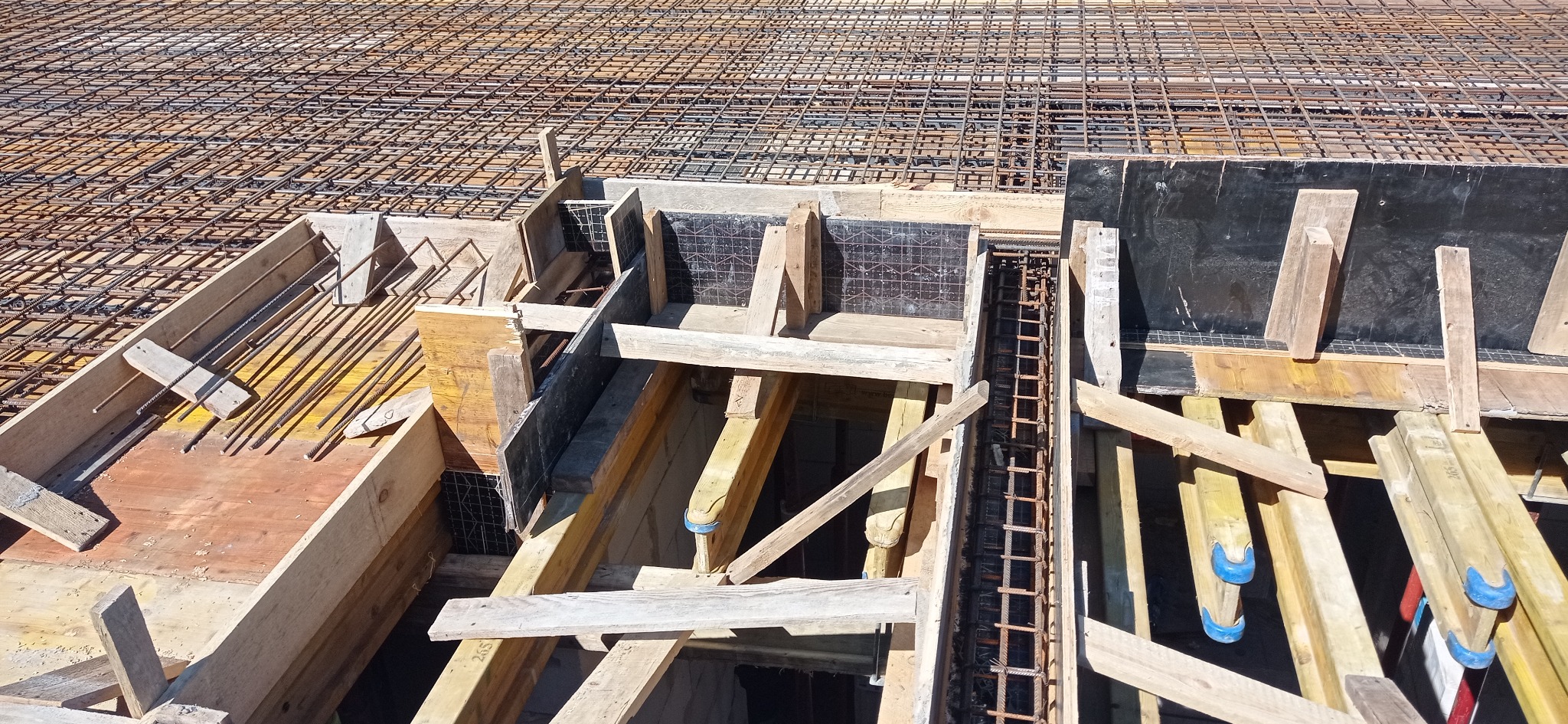 Zbrojenie i szalunki fundamentów pod budowę w Warszawie. Widoczne drewniane konstrukcje i siatka z prętów stalowych, przygotowane do zalania betonem.