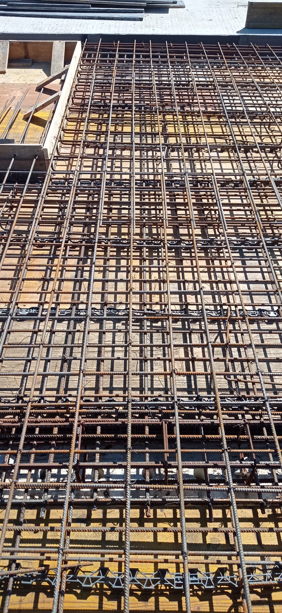 Zbrojenie fundamentu z widocznymi elementami dystansowymi na deskowaniu. Widok z góry ukazuje siatkę prętów zbrojeniowych przygotowaną do zalania betonem.