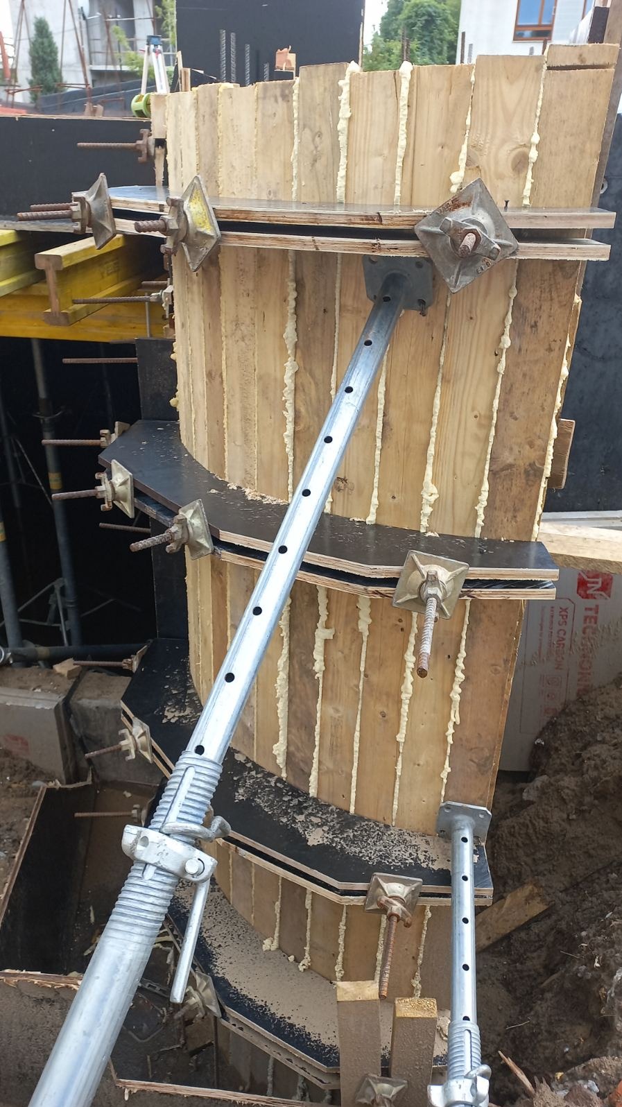 Szczegółowe ujęcie szalunku kolumny z drewnianych desek, wzmocnionego metalowymi rozpórkami i pianką uszczelniającą, na placu budowy. Widoczne elementy zbrojenia.