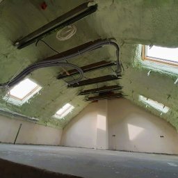 PROteam Rafał Prokopczyk - Poddasze po ociepleniu pianką PUR z widocznymi oknami dachowymi i przewodami instalacyjnymi. Ściany częściowo otynkowane, surowa podłoga.