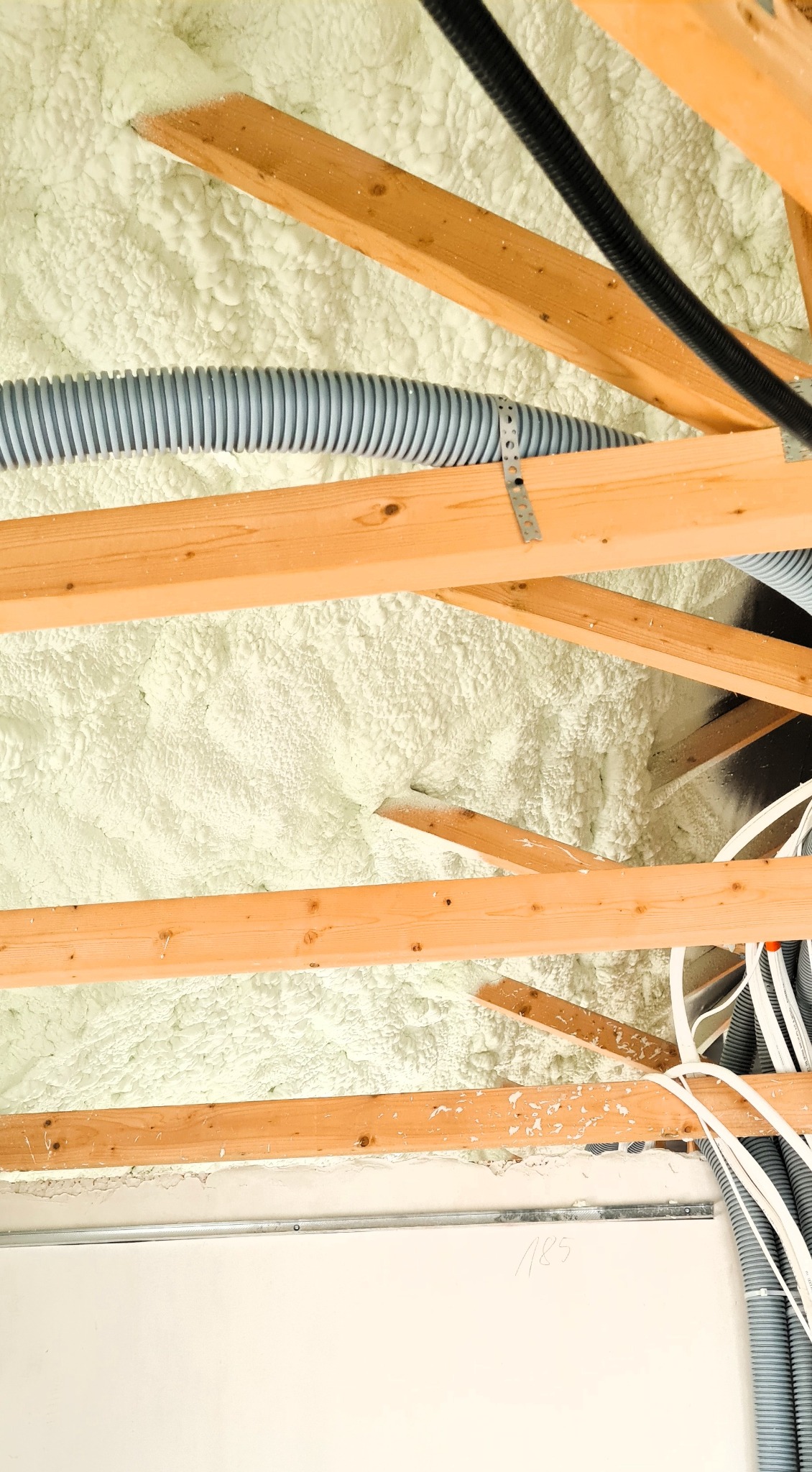 Poddasze po aplikacji pianki PUR w Markach. Widoczne krokwie, instalacje i biała piana izolacyjna wypełniająca przestrzeń, tworząc barierę termiczną.