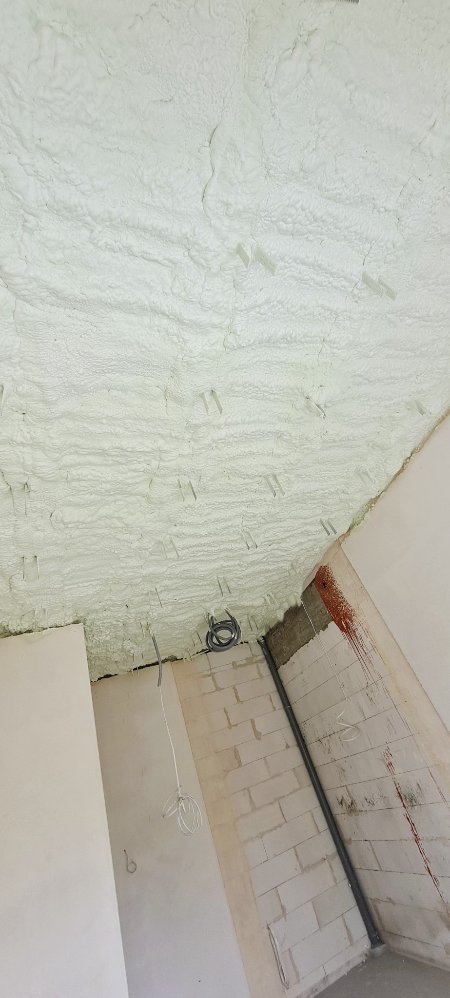 Poddasze po natrysku pianki PUR, widoczne mocowania i fragment instalacji elektrycznej. Ściany z surowej cegły częściowo przygotowane do dalszych prac.