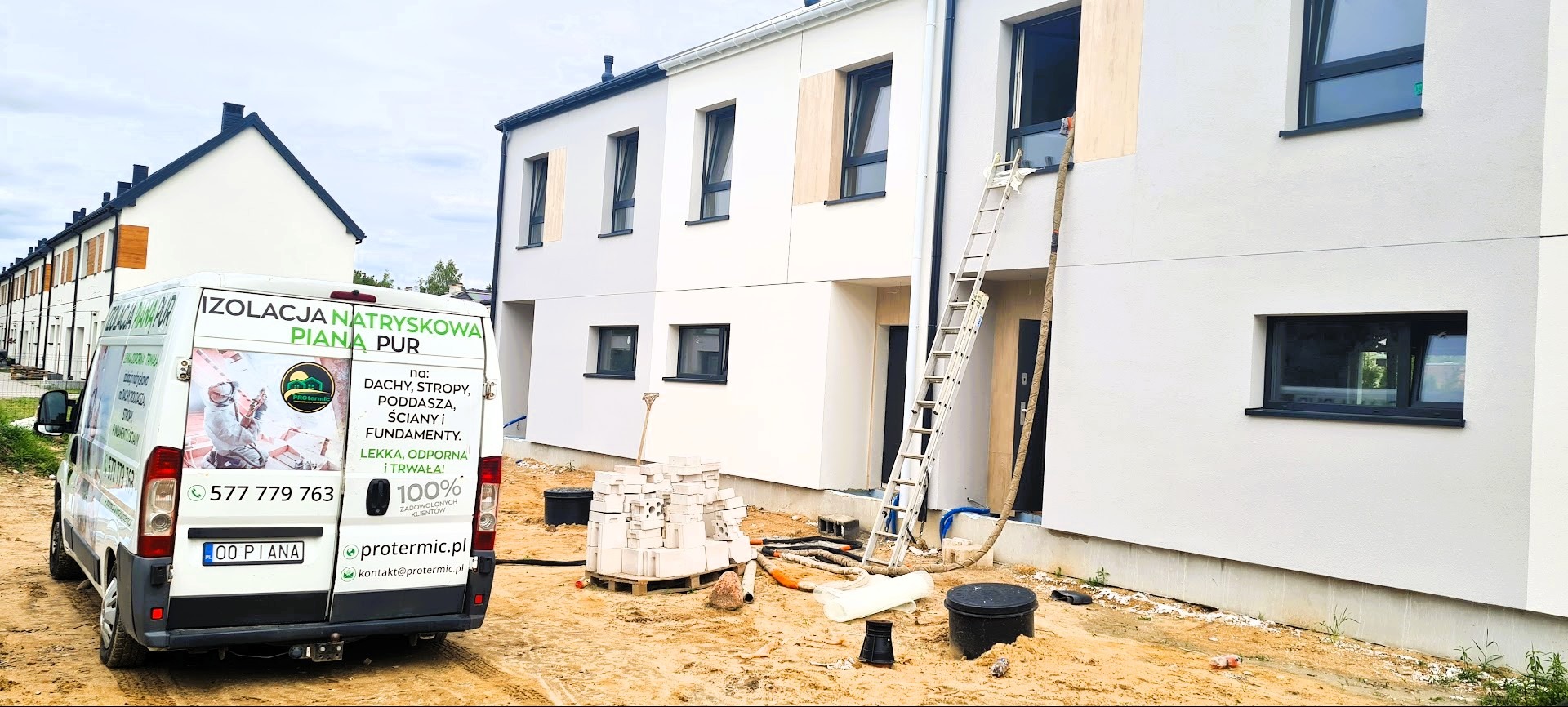 Ściana budynku w trakcie ocieplania, z widoczną drabiną i samochodem firmy z reklamą pianki PUR. Fragmenty ścian bez ocieplenia. Teren budowy.