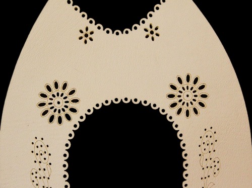 Beżowa skóra z precyzyjnie wyciętymi laserowo wzorami kwiatowymi i brzegami, ukazująca detale obróbki CNC na ciemnym tle.