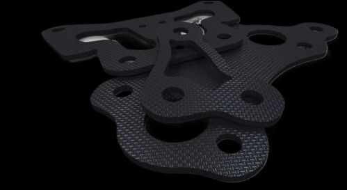 Czarne, precyzyjnie wycięte laserowo elementy z tworzywa technicznego o wzorze karbonu, ułożone warstwowo na czarnym tle. Detal obróbki materiałów.