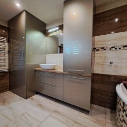 Wymiarowe Meble Marcin Sekular - Nowoczesna, szara zabudowa łazienkowa z umywalką nablatową i wysokimi szafkami, dopasowana do płytek w odcieniach brązu i beżu. Całość dopełnia lustro.