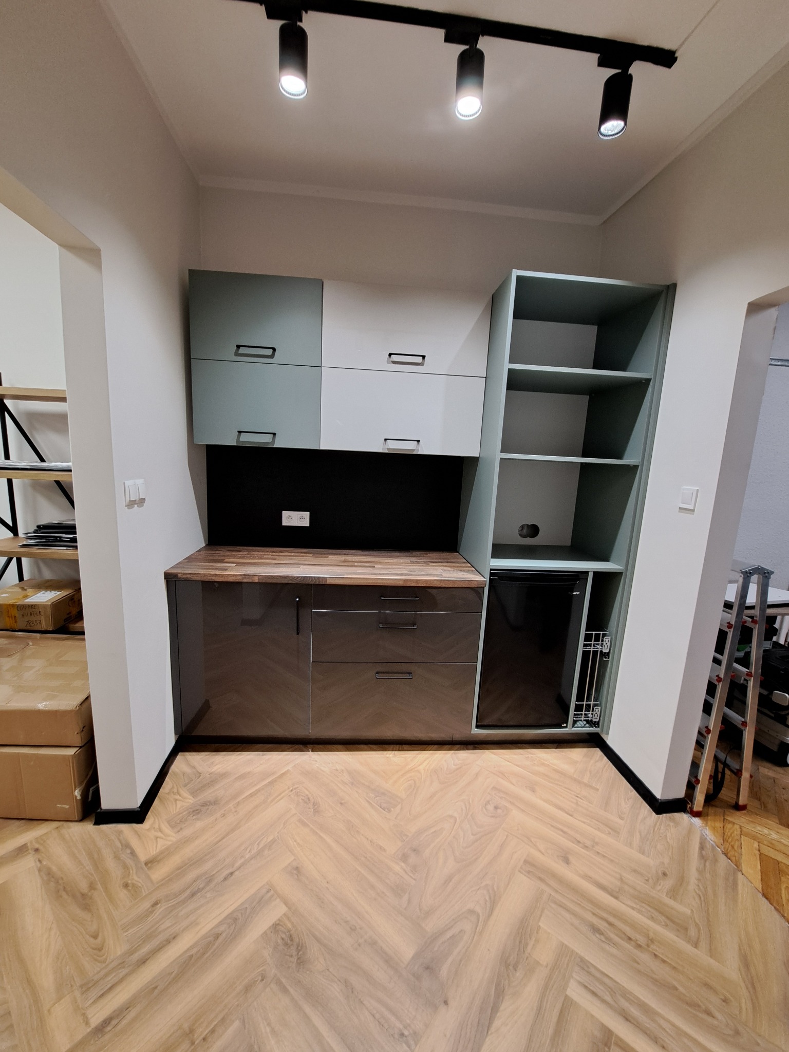 Nowoczesna zabudowa kuchenna z szafkami w odcieniach szarości i drewna, z wbudowaną lodówką i oświetleniem punktowym. Parkiet ułożony w jodełkę.