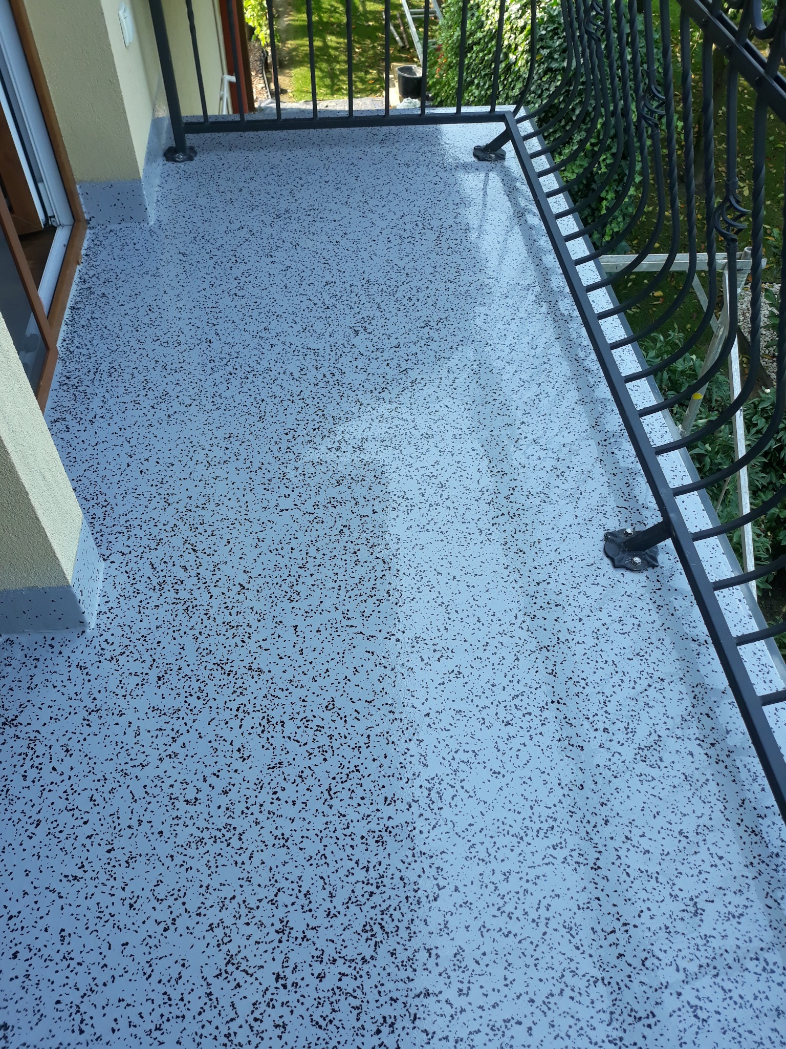 Szara, żywiczna posadzka balkonu z czarnymi drobinkami, widok z góry, z barierką. Gładka powierzchnia z subtelnym połyskiem, świeżo po aplikacji.