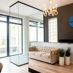 Eleganckie wnętrze recepcji kliniki z beżową sofą chesterfield, szklaną ścianką i widokiem na ogród przez okno. Na ścianie logo kliniki w kolorze niebieskim.