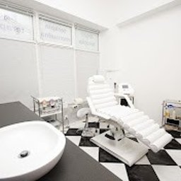 KLINIKA HB Warszawa - Fizjoterapia bólu miednicy - Uroginekologia kobiet i mężczyzn - Jasne wnętrze gabinetu z białym fotelem do zabiegów, umywalką i sprzętem medycznym. Czarno-biała szachownica na podłodze. Minimalistyczny, sterylny wystrój.