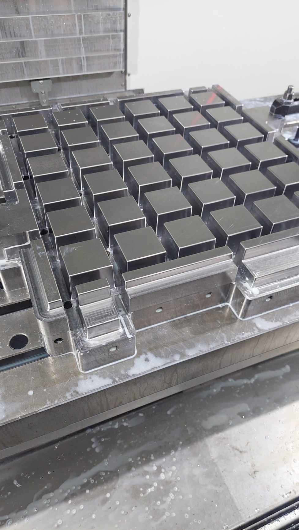 Metalowa matryca z równo rozmieszczonymi, obrobionymi kostkami, prawdopodobnie w trakcie procesu produkcyjnego z widocznymi śladami chłodziwa.