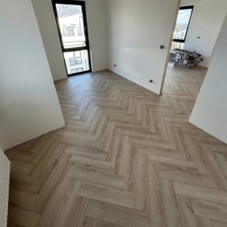 REM-DOM - Jasne panele ułożone w jodełkę francuską w nowym mieszkaniu z oknem i widocznymi narzędziami w tle. Minimalistyczne wnętrze po remoncie.