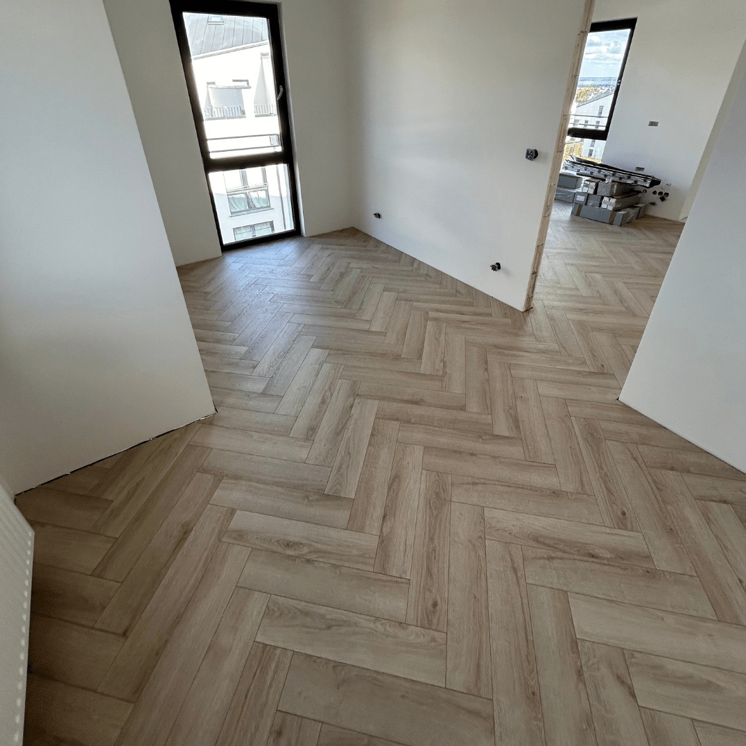 Jasne panele ułożone w jodełkę francuską w nowym mieszkaniu z oknem i widocznymi narzędziami w tle. Minimalistyczne wnętrze po remoncie.