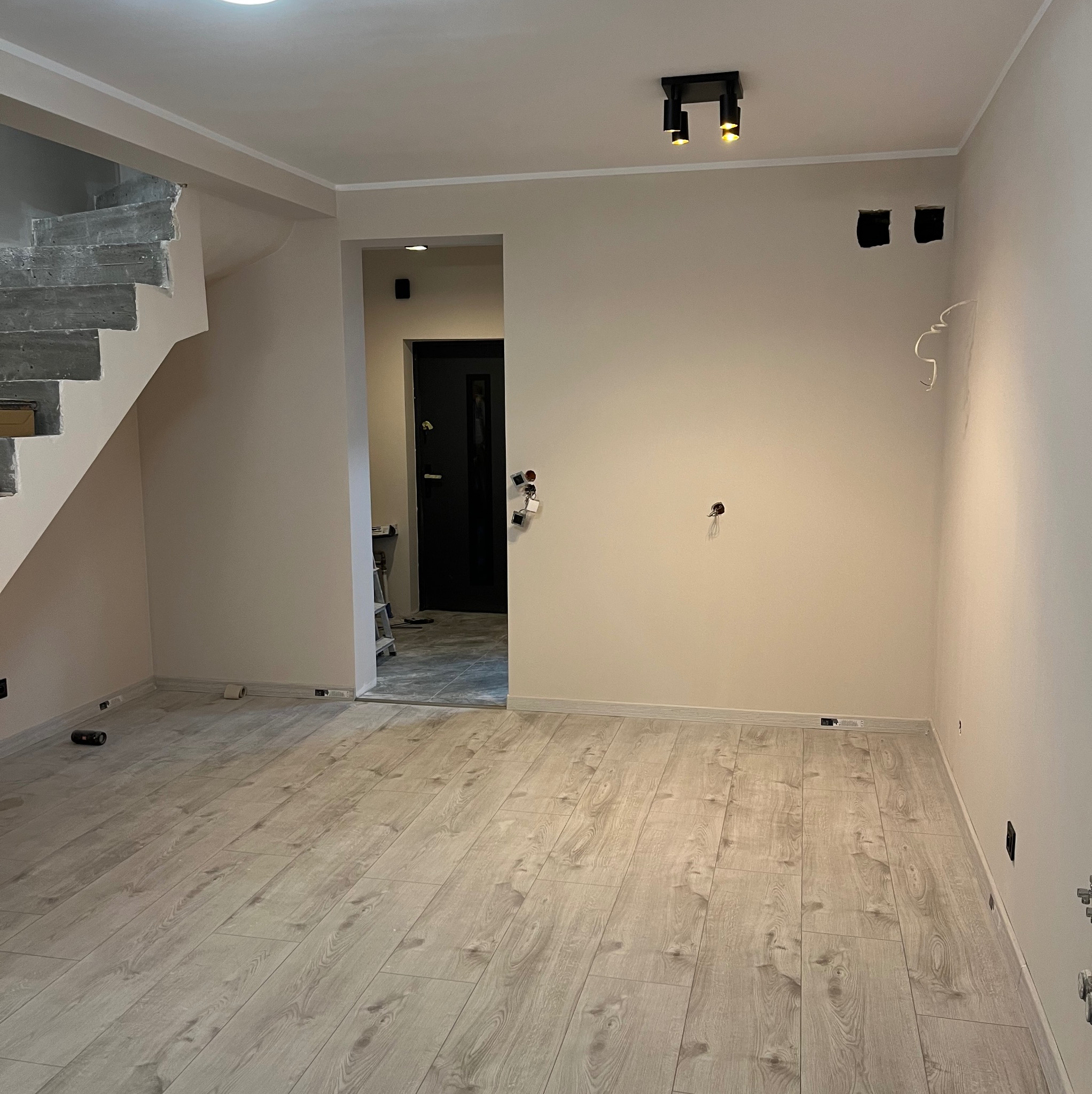 Jasne panele podłogowe w nowym wnętrzu, świeżo pomalowane ściany w odcieniach beżu, widoczne schody w surowym stanie i przygotowane punkty elektryczne.