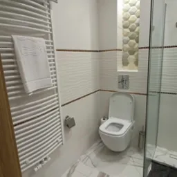 Nowoczesna łazienka z białą armaturą, grzejnikiem drabinkowym z ręcznikami, płytkami z efektem 3D i mozaiką. Marmurowe płytki podłogowe.