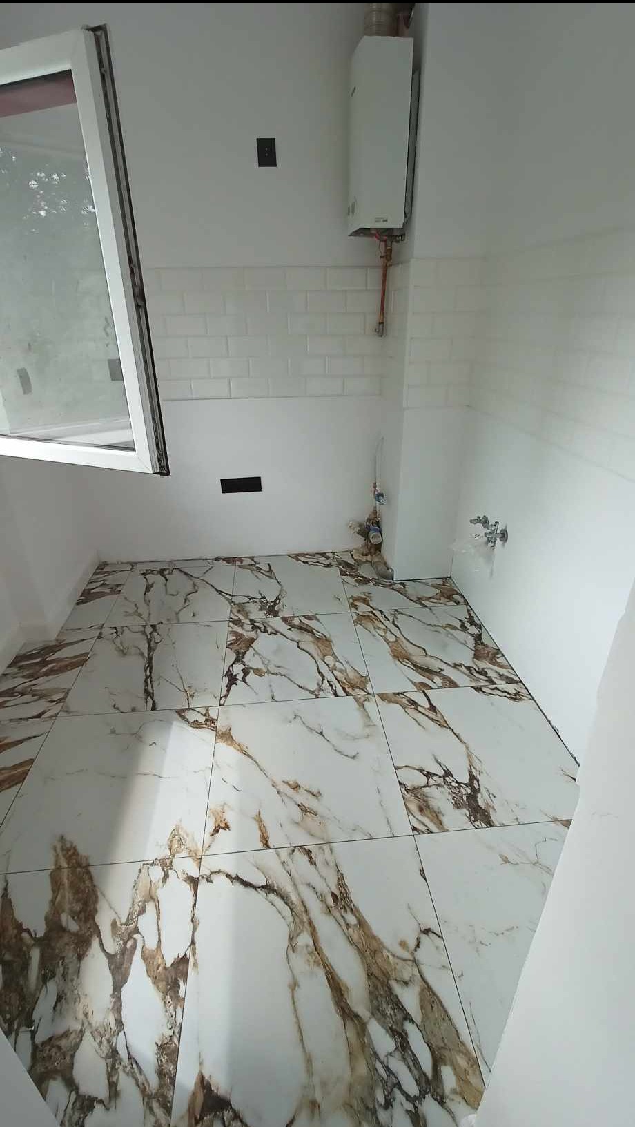 Wykończona łazienka z marmurową podłogą i białą glazurą w Jeleniej Górze. Widoczny bojler i okno. Charakterystyczny wzór płytek podłogowych.